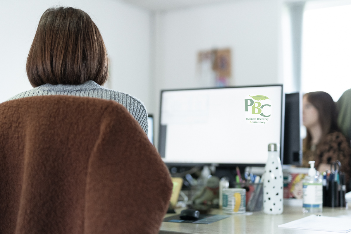 Woman sitting at desk with PBC logo on the screen